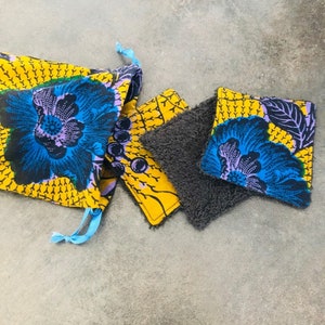 May include: A set of three reusable makeup remover pads. The pads are made of a soft, absorbent material and have a floral print in shades of yellow, blue, and purple. The pads are packaged in a drawstring bag with the same floral print.