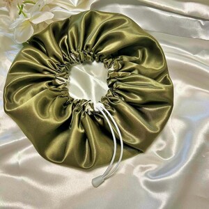 Peut inclure: Un bonnet de nuit en satin vert avec un cordon de serrage blanc. Le bonnet est froncé en haut et a une texture lisse et soyeuse.