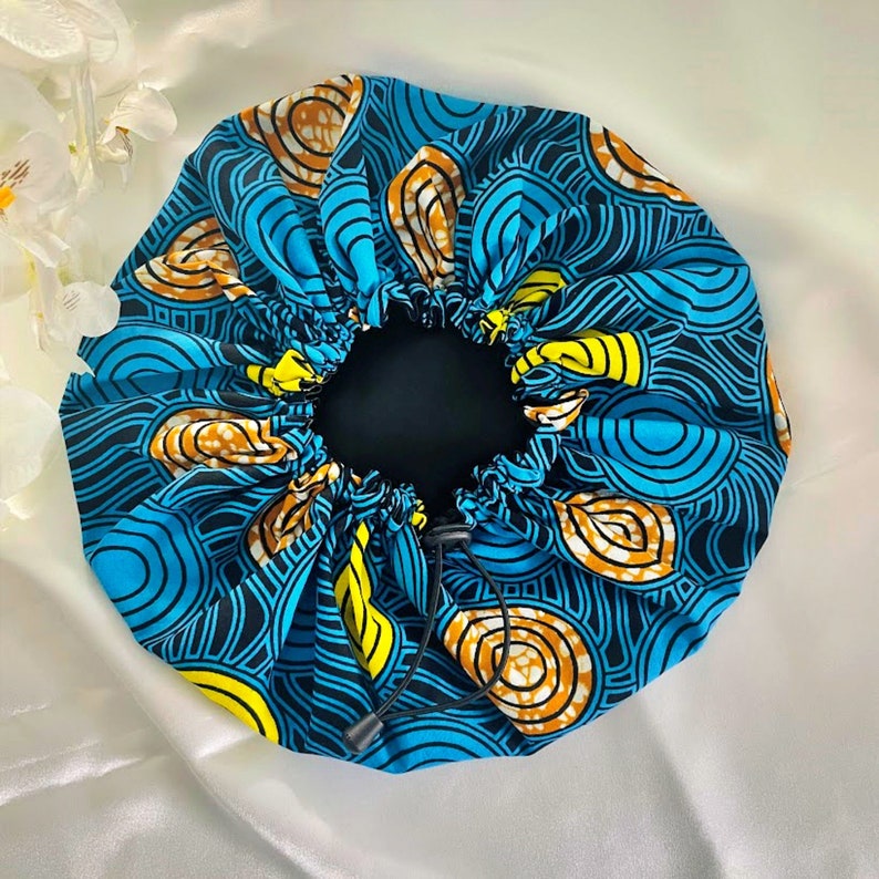 May include: A blue and yellow patterned satin bonnet with a black drawstring. The bonnet is designed to protect hair while sleeping.
