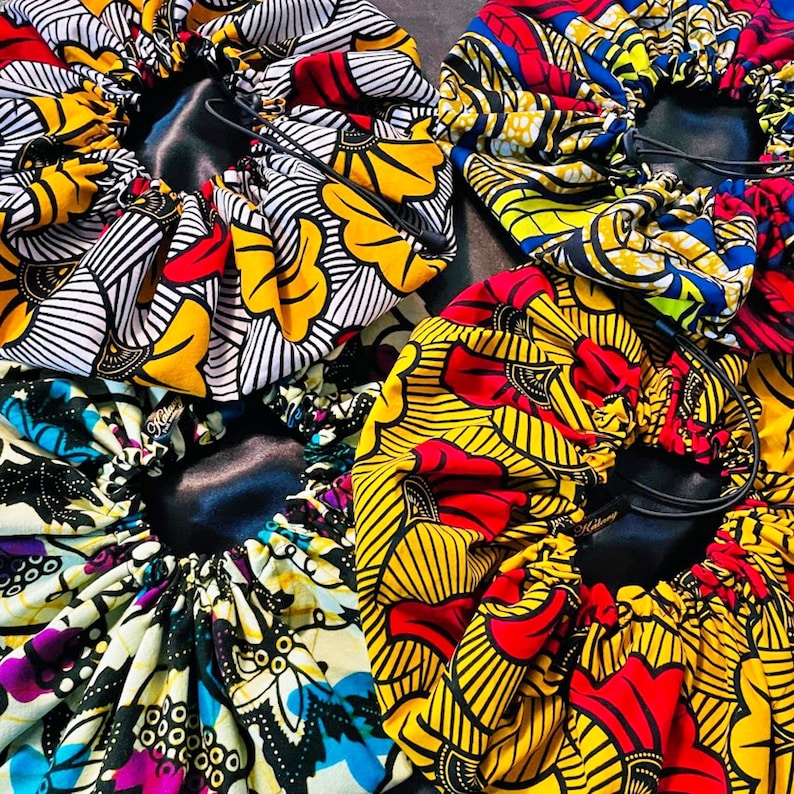 May include: Four colorful satin fabric hair bonnets with elastic bands and drawstrings. The bonnets are in various patterns of yellow, red, blue, and black.