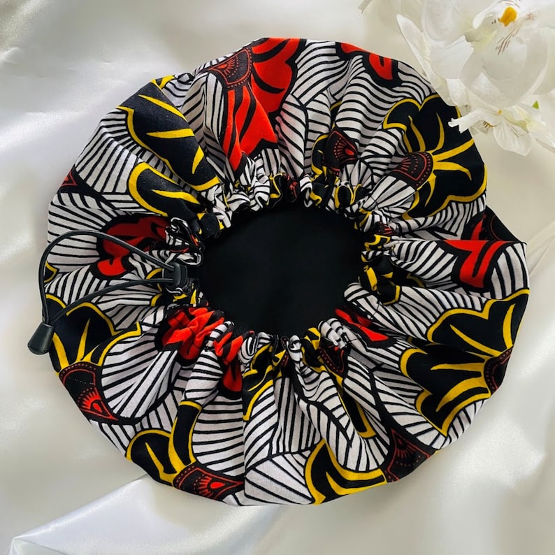 May include: A black, white, red, and yellow patterned satin sleep cap with a drawstring closure.