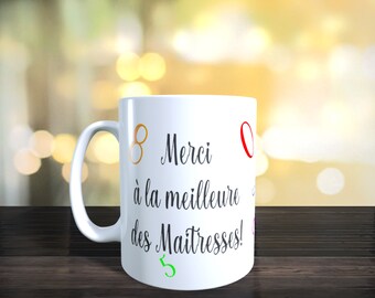 Puede incluir: Taza de cerámica blanca con una inscripción en negro que dice "Merci à la meilleure des Maîtresses!" con números coloridos alrededor del texto.
