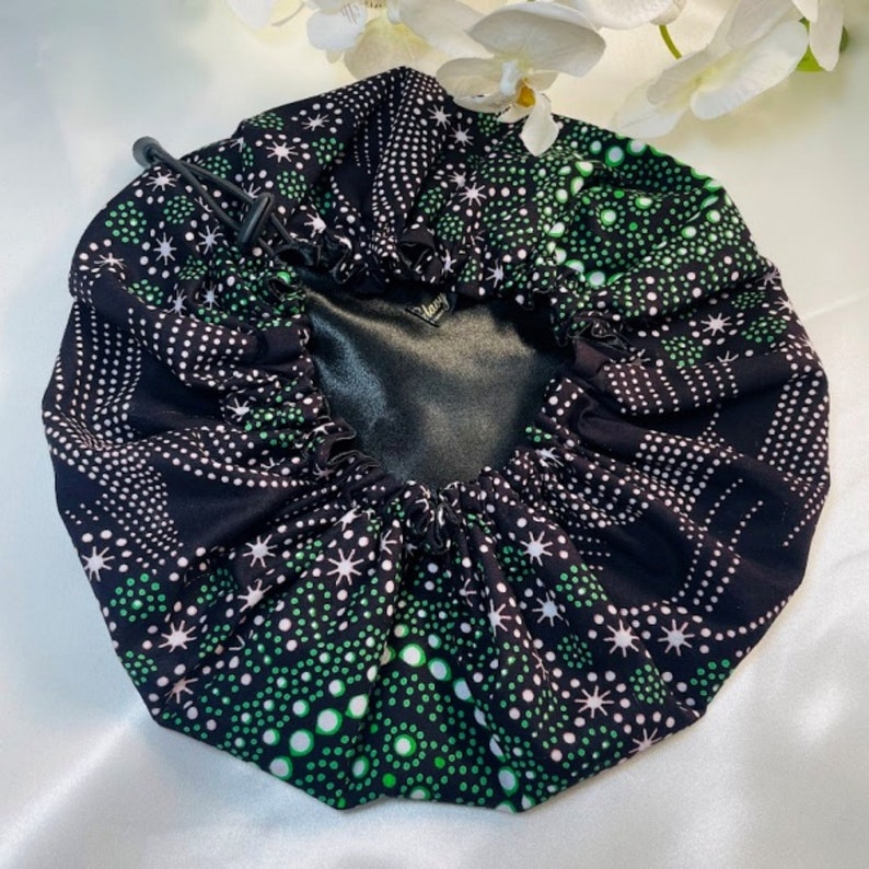 May include: A black satin-lined sleep cap with a green and white polka dot pattern. The cap has a drawstring closure.