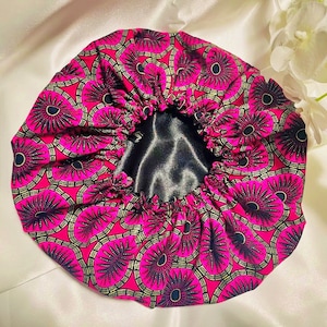 May include: A pink satin bonnet with a black satin lining. The bonnet has a circular pattern of black and gold flowers.