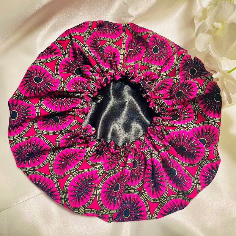 May include: A pink satin bonnet with a black satin lining. The bonnet has a circular pattern of black and gold flowers.