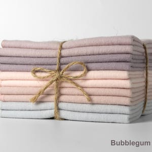 Op de afbeelding: Een stapel gevouwen stoffen vierkanten in roze, lavendel en grijstinten, samengebonden met touw. De tekst "Bubblegum Mix" staat onderaan. De stof ziet er zacht uit en is netjes opgestapeld.
