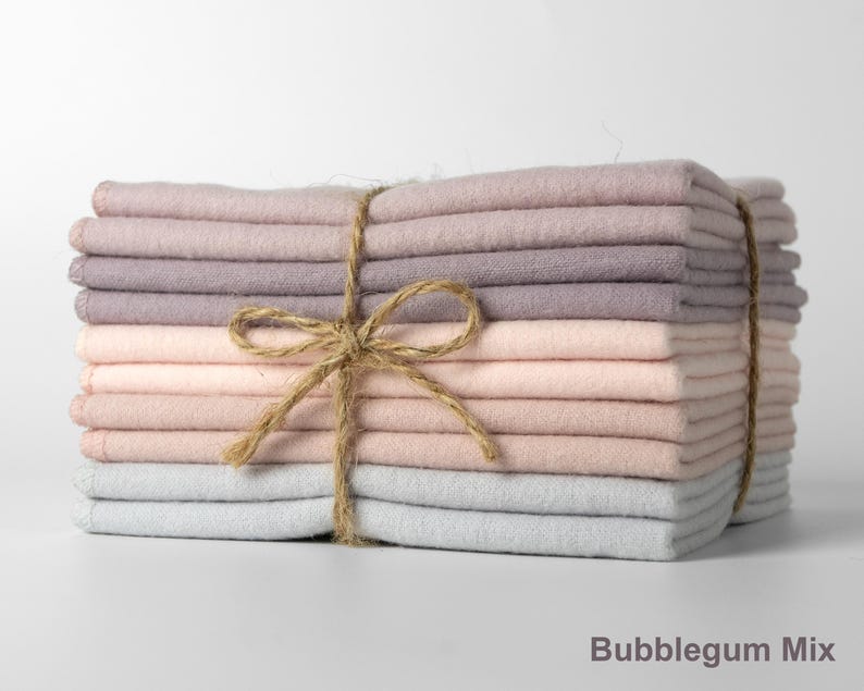 Op de afbeelding: Een stapel gevouwen stoffen vierkanten in roze, lavendel en grijstinten, samengebonden met touw. De tekst "Bubblegum Mix" staat onderaan. De stof ziet er zacht uit en is netjes opgestapeld.