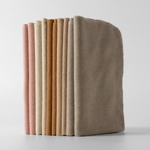 May include: A stack of folded fabric items in various neutral colors, including pink, beige, and brown. The items are neatly arranged, showcasing their different shades and textures. The edges of the fabric are visible, suggesting a soft, possibly absorbent material.