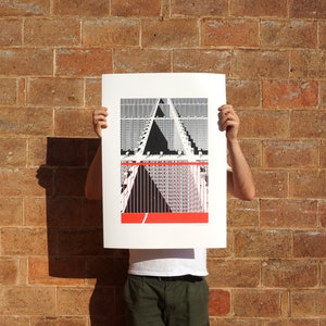 Può includere: Una stampa in bianco e nero di un design geometrico con un accento rosso. La stampa è tenuta davanti a un muro di mattoni.