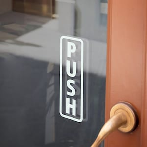 May include: A white "PUSH" sign on a glass door with a brass door handle.
