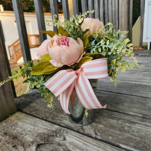 May include: A pink and green floral arrangement in a galvanized metal container with a pink and white striped ribbon.