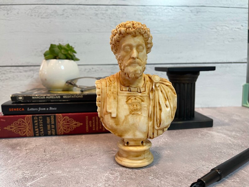 May include: A beige bust sculpture of a man with a beard and curly hair. The bust is on a pedestal and is made of a smooth, textured material.