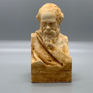 May include: A beige bust sculpture of a man with a beard and a draped cloth. The sculpture is made of a textured material that resembles wood.
