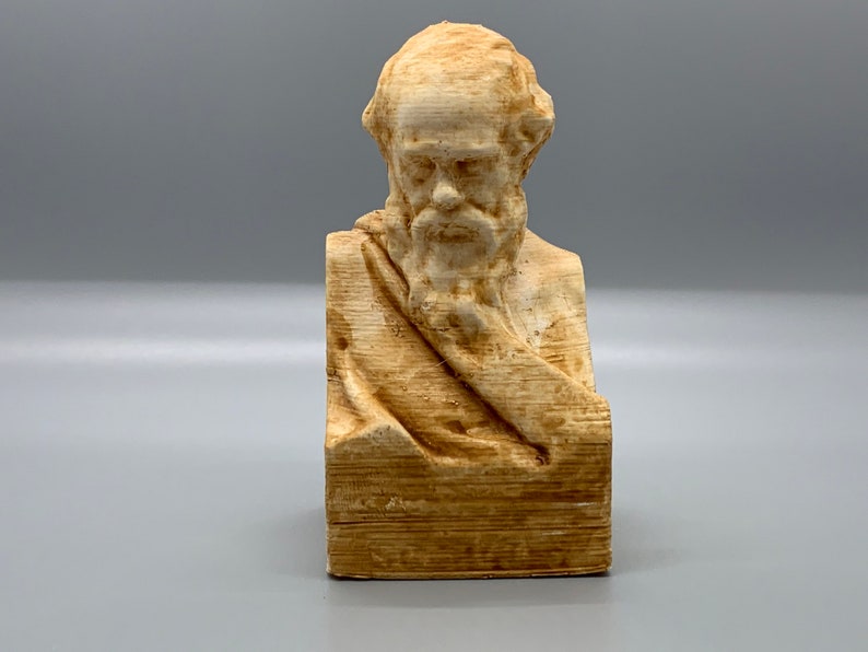 May include: A beige bust sculpture of a man with a beard and a draped cloth. The sculpture is made of a textured material that resembles wood.