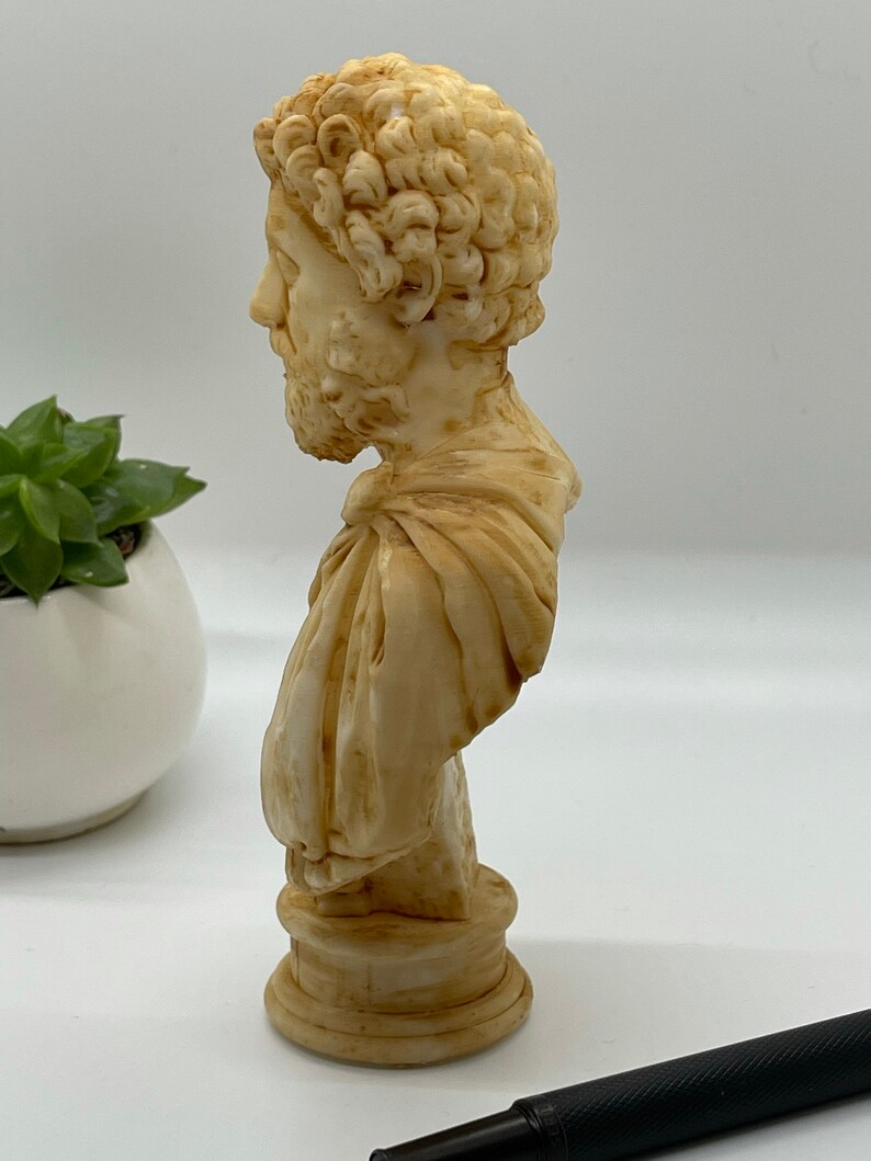 May include: A cream-colored bust sculpture of a man with curly hair and a beard. The bust is on a round base and is made of a smooth material.