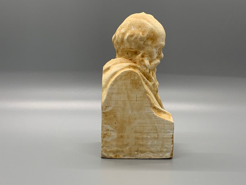 May include: A beige plaster bust of a bearded man with a detailed face and hair. The bust is on a rectangular base.