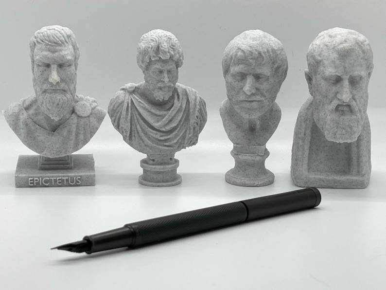 Puede incluir: Cuatro peque&ntilde;os bustes de yeso blanco de figuras hist&oacute;ricas, incluyendo Epicteto, sobre una superficie blanca con un bol&iacute;grafo negro.