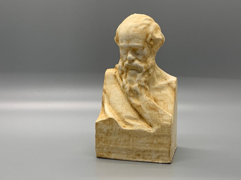 May include: A beige bust sculpture of a man with a beard and a draped cloth. The sculpture is made of a textured material and has a slightly weathered appearance.