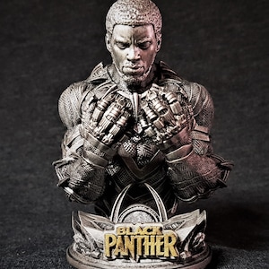 May include: A silver-finished bust of Black Panther. The sculpture shows detailed features of the character's suit and a base with the words "Black Panther" in gold lettering. This bust is a collectible item.