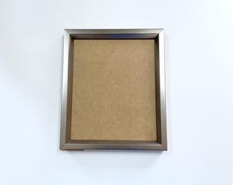 May include: A silver picture frame with a brown cardboard backing.