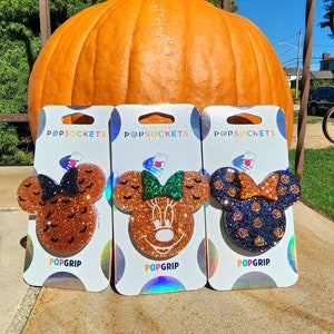 May include: Three Halloween-themed PopSockets phone grips featuring a Mickey Mouse silhouette with different glitter patterns. The first grip has orange glitter with black bats, the second has brown glitter with green bow and the third has black glitter with orange pumpkins.