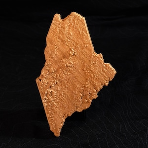 May include: A gold-colored, three-dimensional map of the state of Maine. The map is textured to show the state's topography.