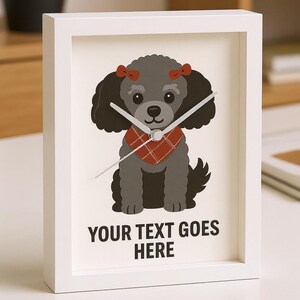May include: White framed clock featuring a cartoon dog with a gray body, black fur, and red bow accents. The dog wears a red plaid scarf. The clock face has the text "YOUR TEXT GOES HERE".
