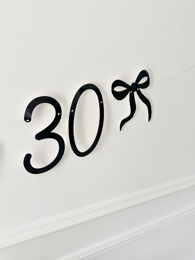 May include: Black metal number 30 with a bow accent, perfect for a birthday or anniversary celebration. The numbers are in a bold, cursive font, and the bow adds a decorative touch. Ideal for party decorations.