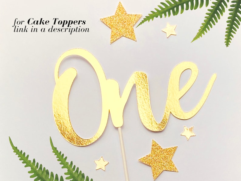 May include: Gold glitter cake topper with the word "One" in a cursive font. The topper is surrounded by small gold glitter stars.