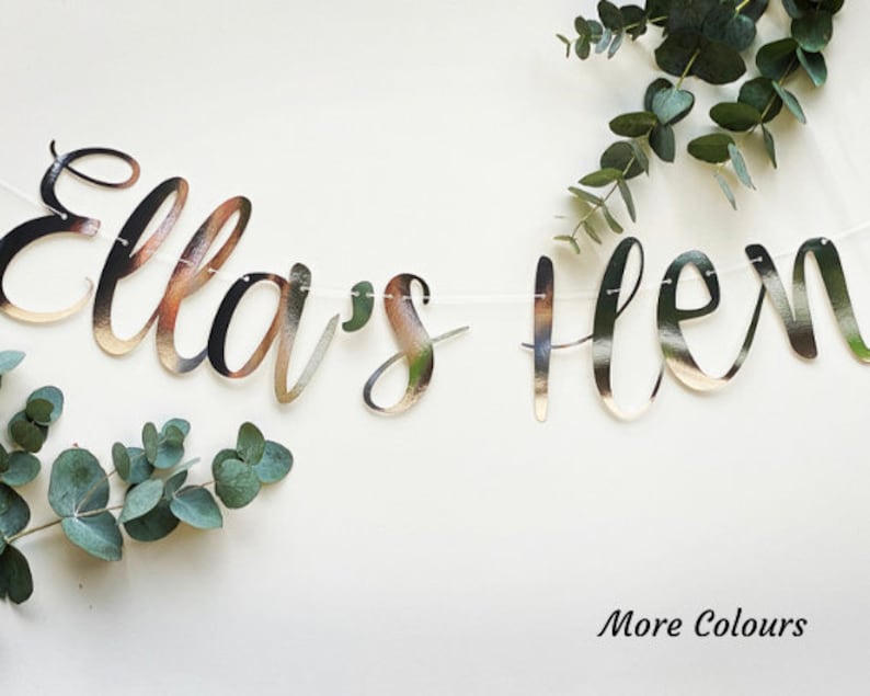 May include: A silver glitter banner with the text "Ella's Hen" in cursive script. The banner is strung with white thread and is decorated with eucalyptus leaves.