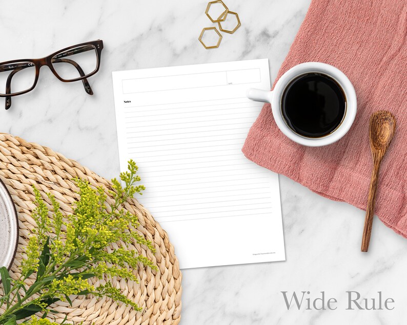 May include: A white sheet of paper with wide ruled lines. The paper is on a marble surface with a cup of coffee, a wooden spoon, a woven placemat, a sprig of yellow flowers, and gold hexagonal shapes.