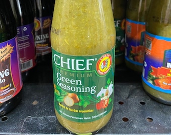 May include: A glass bottle of green seasoning with a white label that says "CHIEF PREMIUM Green Seasoning" and "Aobo de hierbas aromáticas" with a picture of herbs and spices. The bottle is 300 ml.