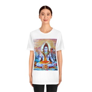 May include: White t-shirt with a colorful image of Shiva, a Hindu deity, sitting on a tiger. Shiva is blue with a third eye and is holding a trident. He is surrounded by mountains and a waterfall.