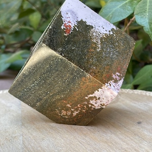May include: A geometric concrete planter with a green, white, and orange speckled finish. The planter is shaped like a cube with rounded edges.