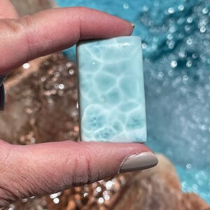 May include: A light blue and white polished stone with a swirling pattern. The stone is rectangular and has a smooth surface.