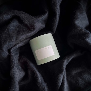 May include: A green candle with a white label that says "COAX" and "SOY WAX CANDLE" on a black fabric background.