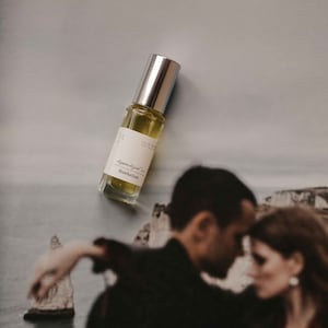 Puede incluir: Un pequeño frasco de perfume de vidrio con una tapa plateada. La etiqueta dice "Apocrypha - Manhattan" y "Eau de Parfum".