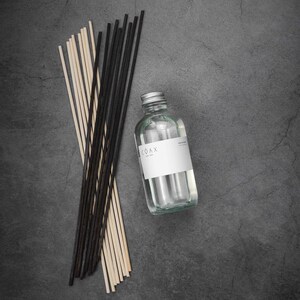 May include: A clear glass bottle with a silver cap and a white label that says "COAX" on it. The bottle is filled with a clear liquid and is surrounded by a bundle of black and natural wooden sticks.