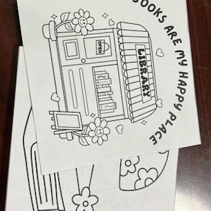 May include: Black and white line art of a library with the text "BOOKS ARE MY HAPPY PLACE". The illustration includes flowers, hearts, and a sign that says "OPEN". The image is on a white paper.