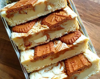 May include: Four slices of white chocolate and biscuit cheesecake, layered in a silver tray. Each slice has a swirl of caramel and a biscuit on top.