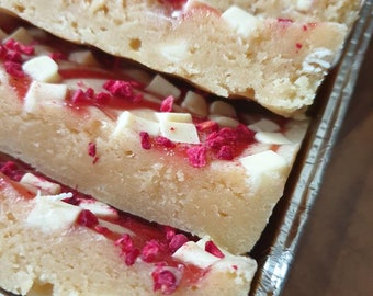 May include: A close-up of a tray of white chocolate raspberry bars. The bars are layered with white chocolate chips and raspberry jam.