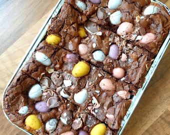 May include: A tray of chocolate brownies topped with mini chocolate eggs. The brownies are cut into squares and the eggs are scattered across the top.