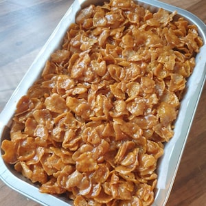 May include: A close-up of a baking dish filled with golden brown cereal squares covered in a caramel sauce.