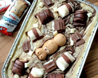 May include: A square aluminum pan filled with a swirl of brown and white batter topped with chocolate and white chocolate candy bars, and a Kinder Happy Hippo biscuit.