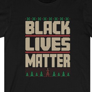 May include: Black T-shirt with a Christmas sweater design featuring the words "Black Lives Matter" in a beige knit font with green and red accents.