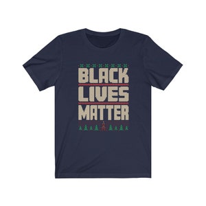 May include: Navy blue t-shirt with a white knit pattern that reads "Black Lives Matter". The pattern includes small green trees and a red figure.