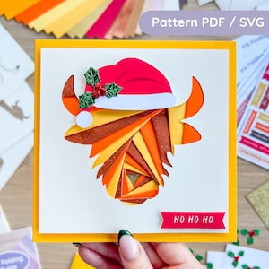May include: A handmade Christmas card featuring a layered paper design of a Highland cow wearing a Santa hat. The card has a yellow border and the text "HO HO HO" on a red banner. The image also includes the text "Pattern PDF / SVG".