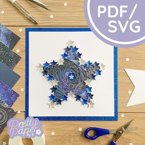 May include: A blue and white paper star with a galaxy design. The star is surrounded by smaller blue and silver stars. The star is on a white card with a blue border. The card is on a wooden surface. The text "Pretty Paper By B" is in the lower left corner of the image. The text "PDF/SVG" is in the upper right corner of the image.