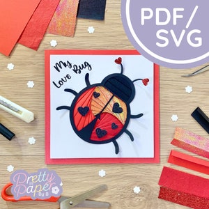 May include: A red and black papercraft ladybug with the words "My Love Bug" on a white card with a red border. The card is surrounded by craft supplies, including red and black paper, glitter paper, and white flowers.