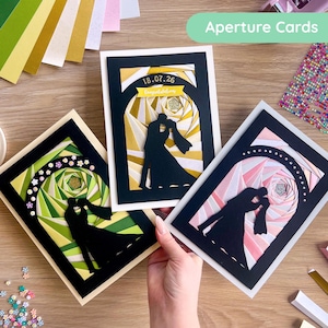 May include: Three handmade wedding cards with black silhouettes of a couple kissing. The cards feature geometric designs in shades of green, yellow, and pink. The text "Aperture Cards" is visible.